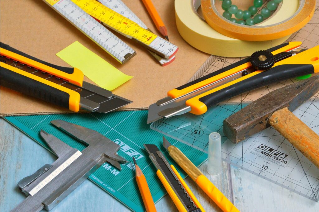 A variety of crafting tools including cutters, ruler, and tape on a work desk.